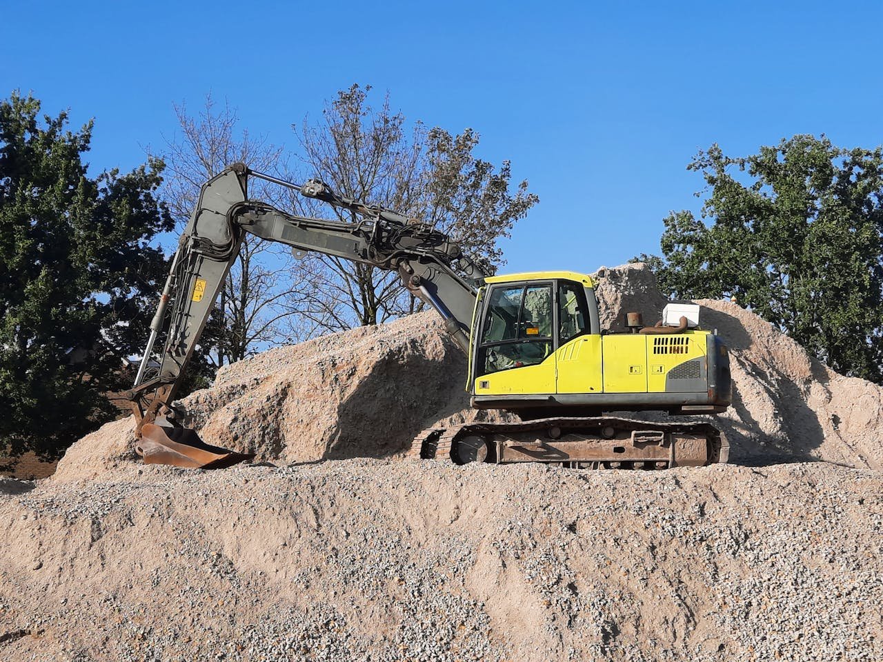 our-story A yellow excavator working on a gravel mound at a construction site.